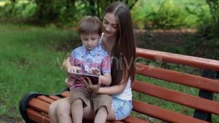 Mother Sitting With Her Son on a Park Bench and Play Tablet
